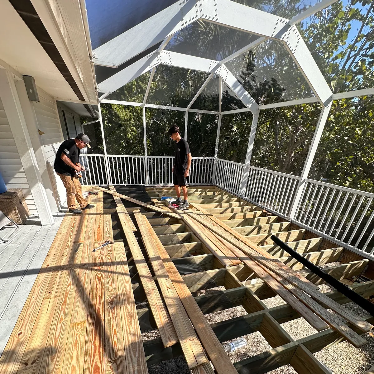 The Grain & Co. crew laying deck boards over a new frame inside a screened pool enclosure