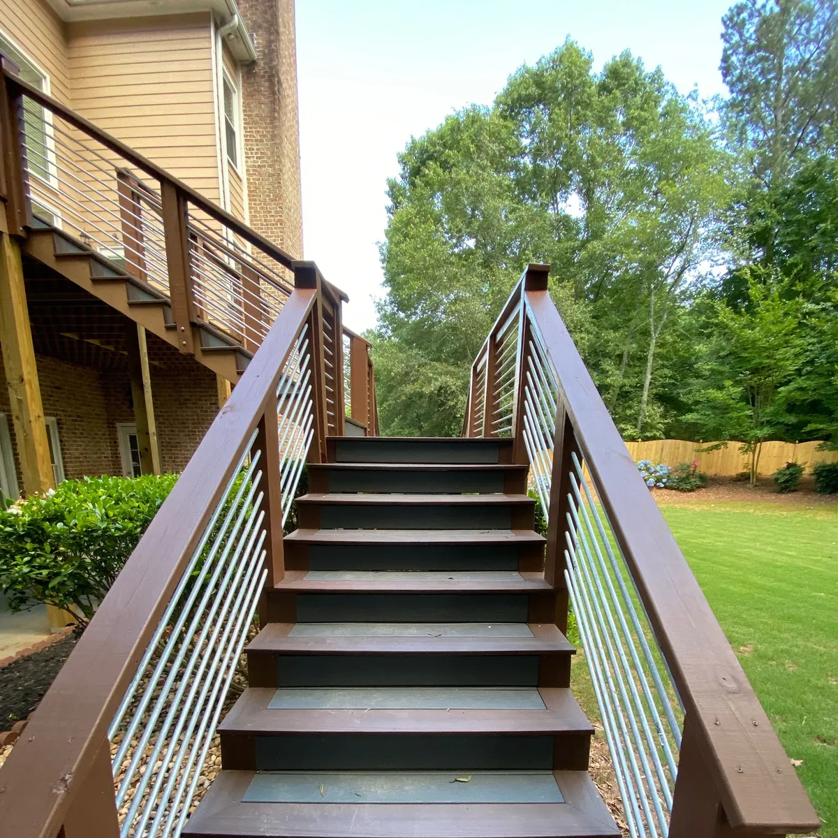 Dark-stained deck stairs with a wood-topped cable railing running down to a lawn