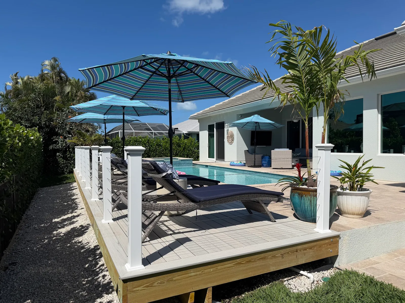 A composite pool deck with white posts and loungers, palms and a screened lanai behind