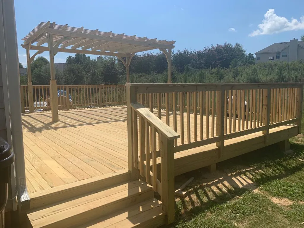 A pressure-treated deck with a pergola over one end, open field behind